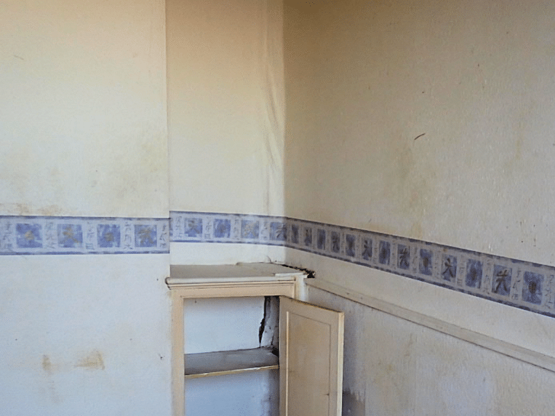 A house with internal cracking partly hidden by a cupboard and wallpaper